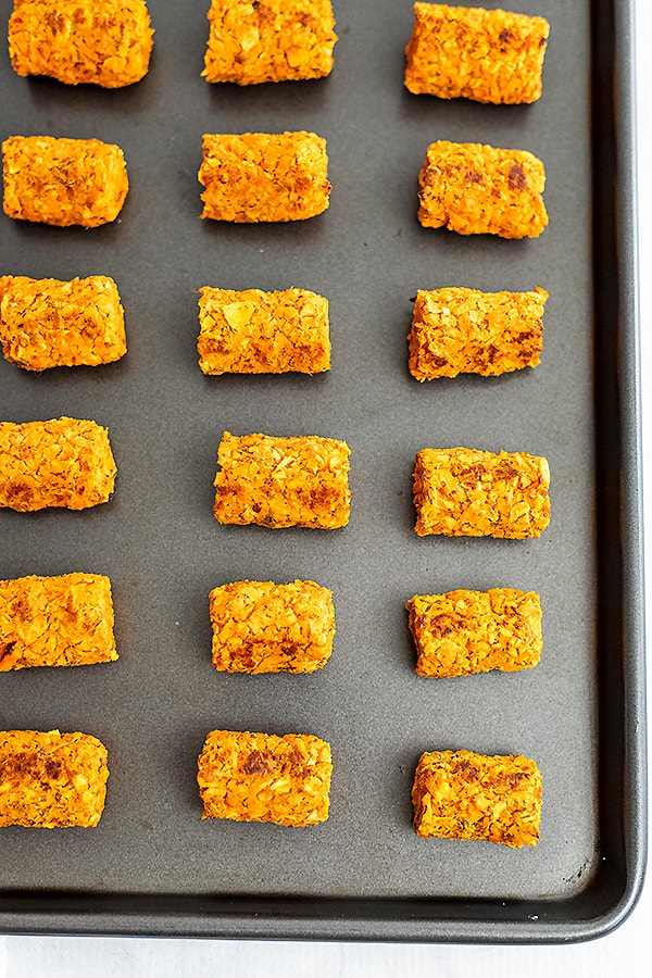 Sweet potato tots lined up on a silver baking sheet after baking.