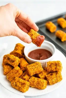 Hand holding sweet potato tot that has been dipped in ketchup