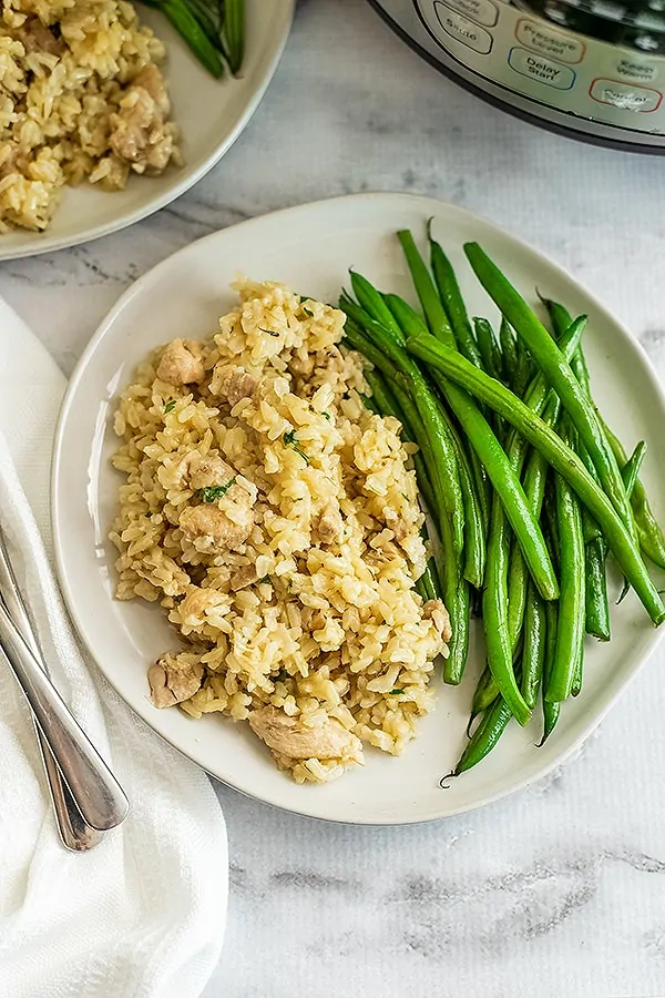 White plate filled with instant pot chicken and rice and green beans.