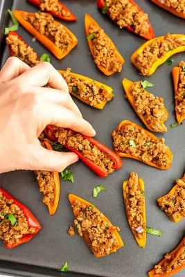 Hand grabbing a mini pepper nacho from the tray.