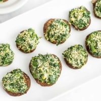Large white plate filled with spinach artichoke stuffed mushrooms.