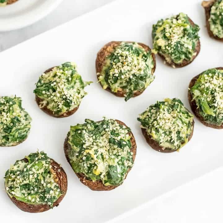 Large white plate filled with spinach artichoke stuffed mushrooms.