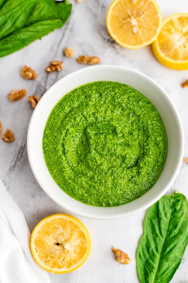 Large bowl of spinach walnut pesto with lemons and basil around bowl.