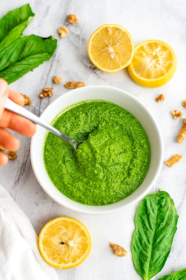 Hand holding a spoon dipping into the bowl of spinach pesto.