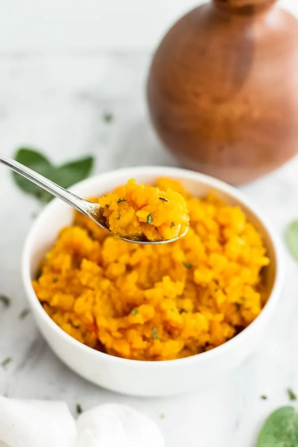 Spoon with a serving of butternut squash risotto from a bowl. 