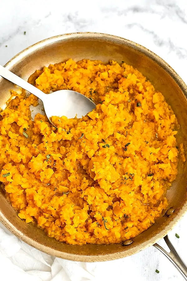 Serving spoon in a skillet filled with butternut squash risotto.