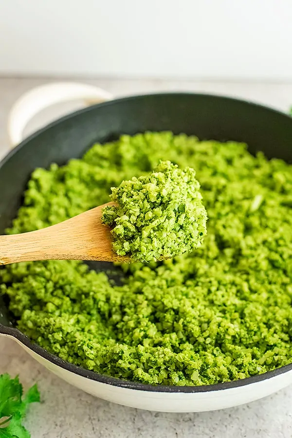Wooden spoon scooping green cauliflower rice from a skillet.