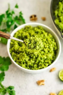 Spoon scooping green cauliflower rice from a white bowl.