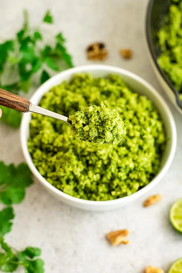 Spoon scooping green cauliflower rice from a white bowl. 
