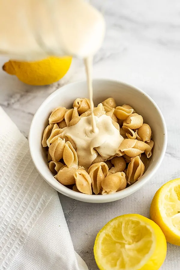Creamy lemon tahini pasta sauce being poured over a bowl of pasta.