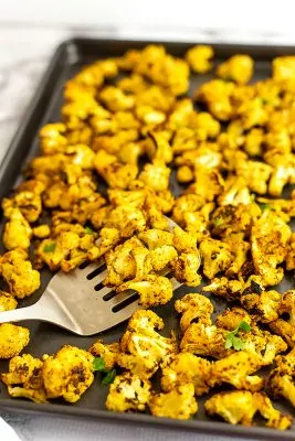 Baking sheet full of Moroccan cauliflower with a silver spatula.