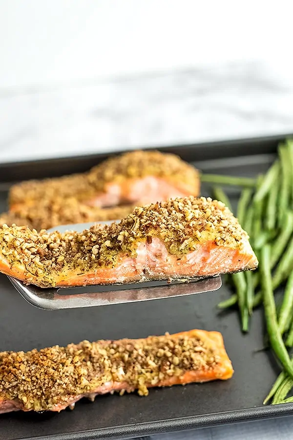 Spatula holding a piece of pecan crusted salmon over sheet pan.