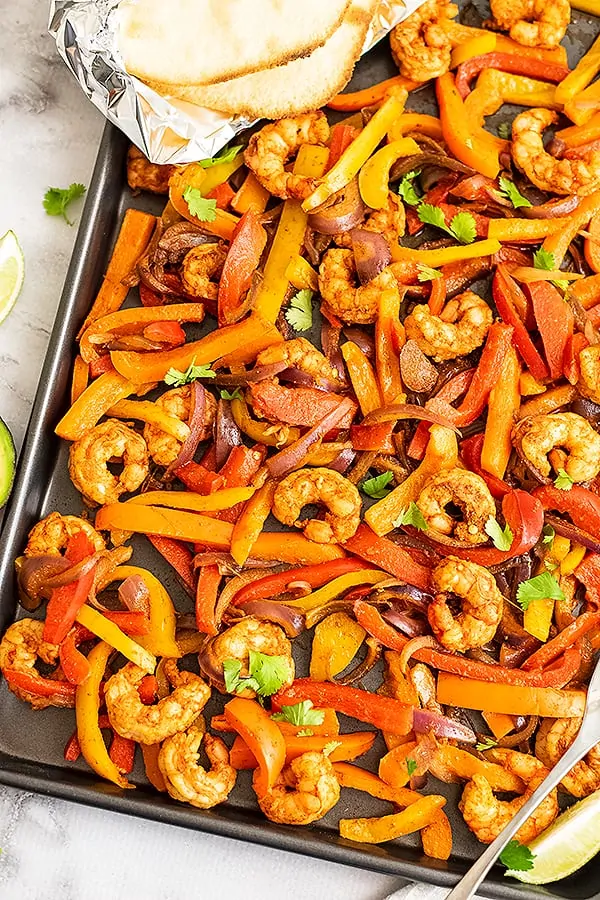 Shrimp fajitas cooked on a sheet pan with tortillas in the corner.
