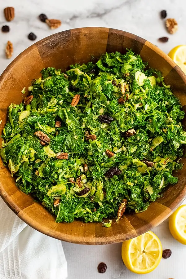 Wooden salad bowl filled with kale brussel sprouts salad with cranberries.