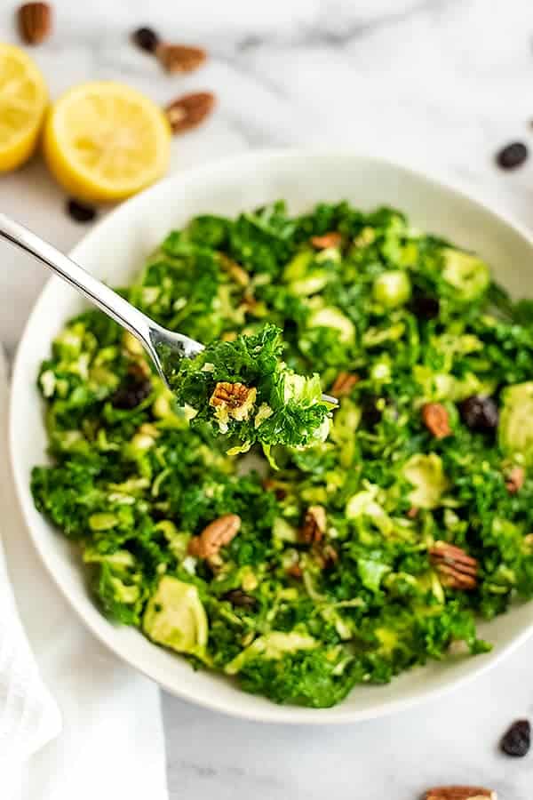 Fork in a white bowl filled with kale brussel sprouts salad.