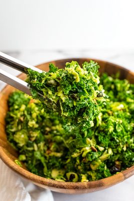 Tongs tossing kale brussel sprouts salad with cranberries.