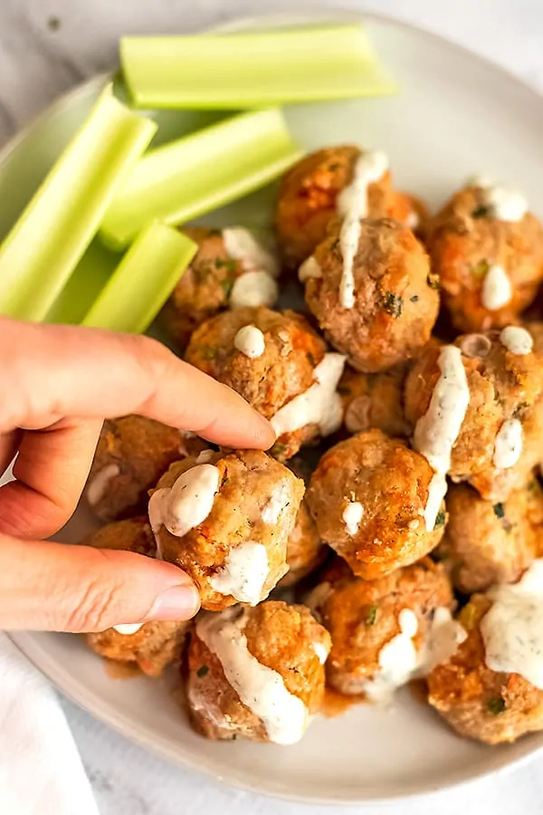 Hand grabbing one buffalo turkey meatball covered in ranch dressing.