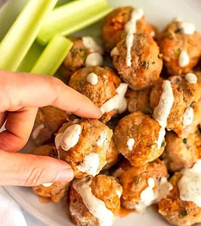 Hand grabbing one buffalo turkey meatball covered in ranch dressing.