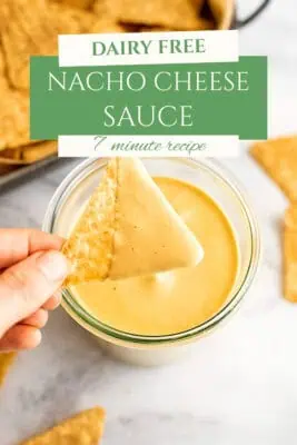 Tortilla chip being dipped in dairy free nacho cheese sauce.