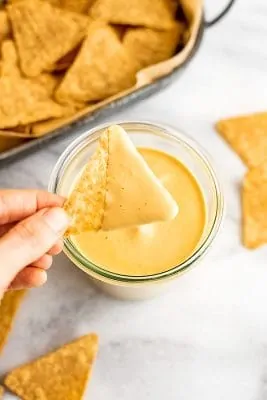 Hand holding chip after being dipped in vegan nacho cheese sauce.