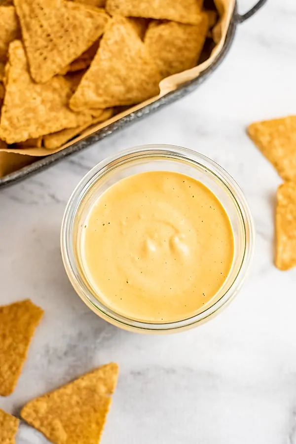 Glass jar filled with cashew queso with chips around the jar.