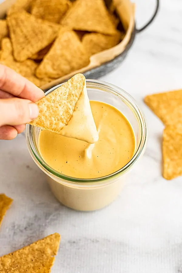 Hand holding a chip after dipping it in cashew queso.