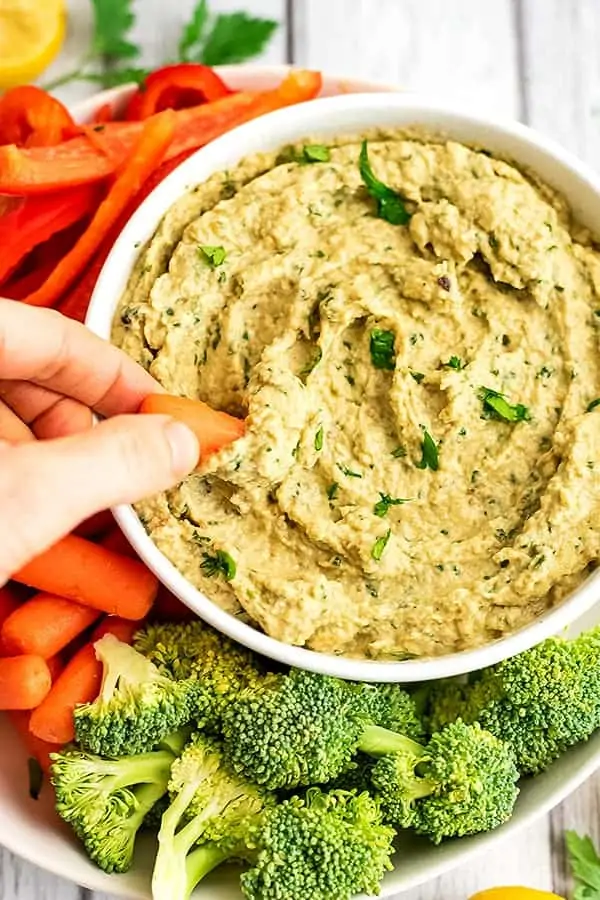 Baby carrot being dipped in bowl of Mediterranean eggplant dip.