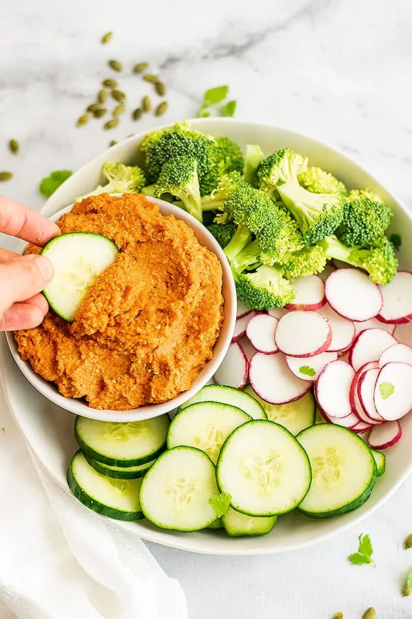 Cucumber being dipped in a bowl of spicy carrot dip.