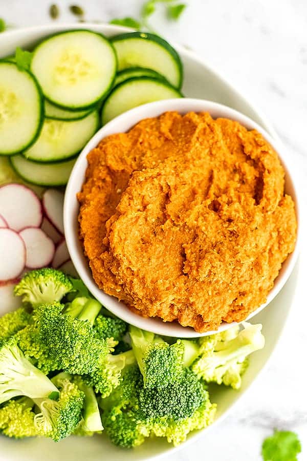 Bowl of spicy carrot dip with veggies on the side.