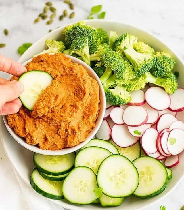 Cucumber being dipped in a bowl of spicy carrot dip.