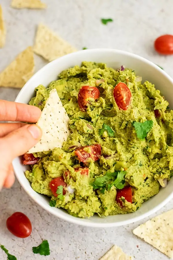 Large bowl of cauliflower guacamole with a chip being dipped in.