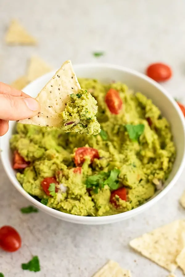 Chip being dipped into a bowl of roasted cauliflower guacamole.