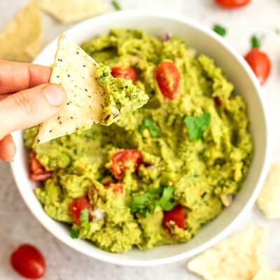 Single tortilla chip being dipped in large bowl of guacamole.