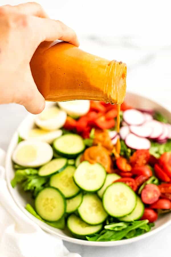 Hand pouring bottle of french dressing over salad.