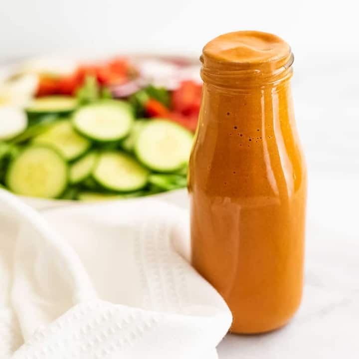 French dressing in a glass bottle with salad in background.