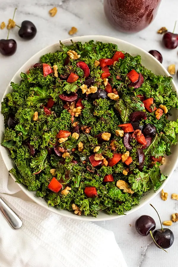 Cherry kale salad in a large white bowl with cherries around the bowl.