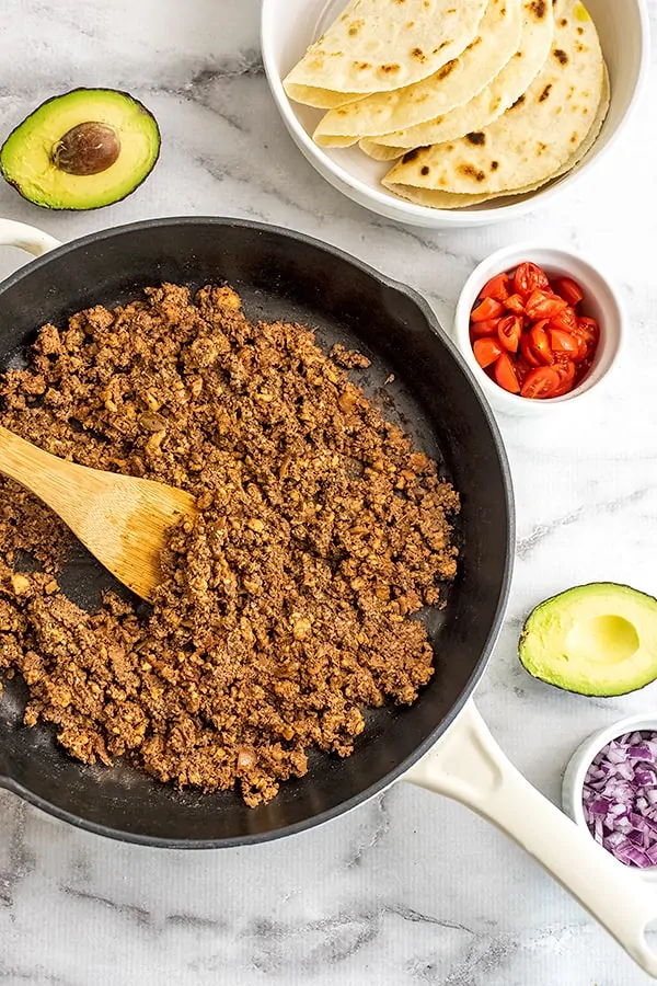 Cast iron skillet with vegan walnut taco meat surrounded by avocado.