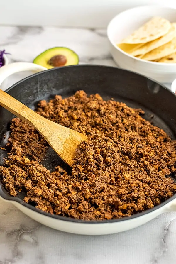 Wooden spoon in skillet with vegan walnut taco meat. 