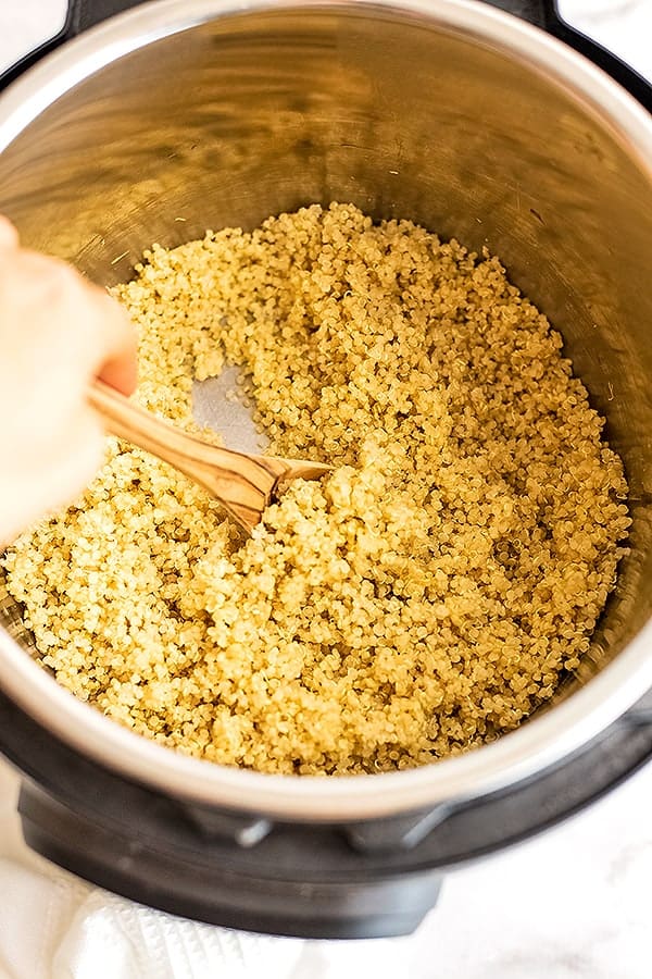 Hand holding spoon stirring quinoa in the instant pot.