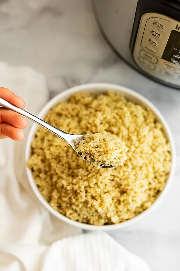 Spoon holding serving of quinoa over a bowl of quinoa.