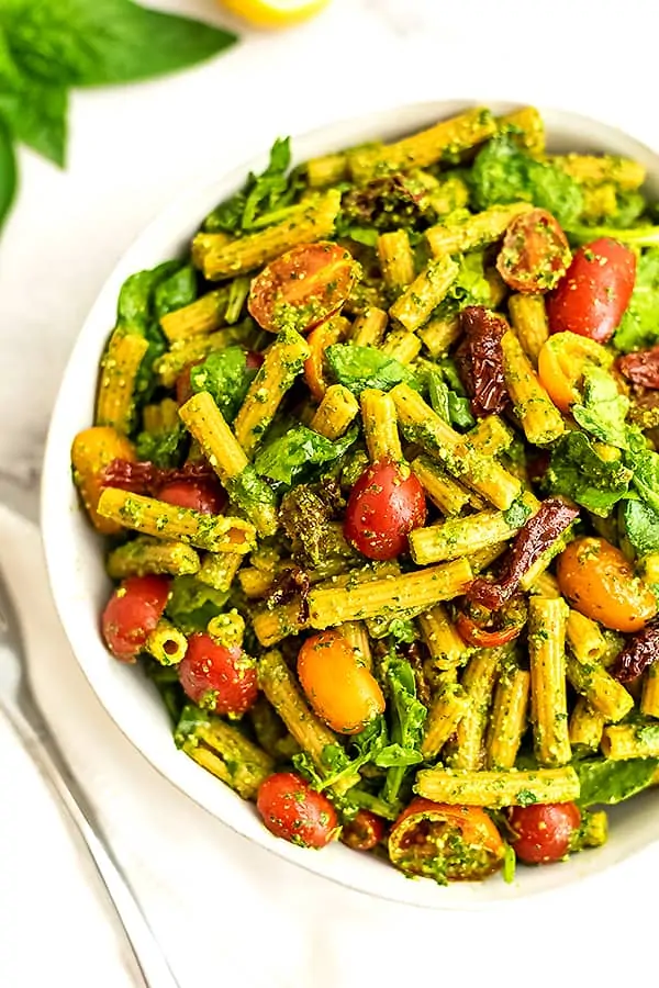 Large bowl filled with pesto pasta salad with sun dried tomatoes.