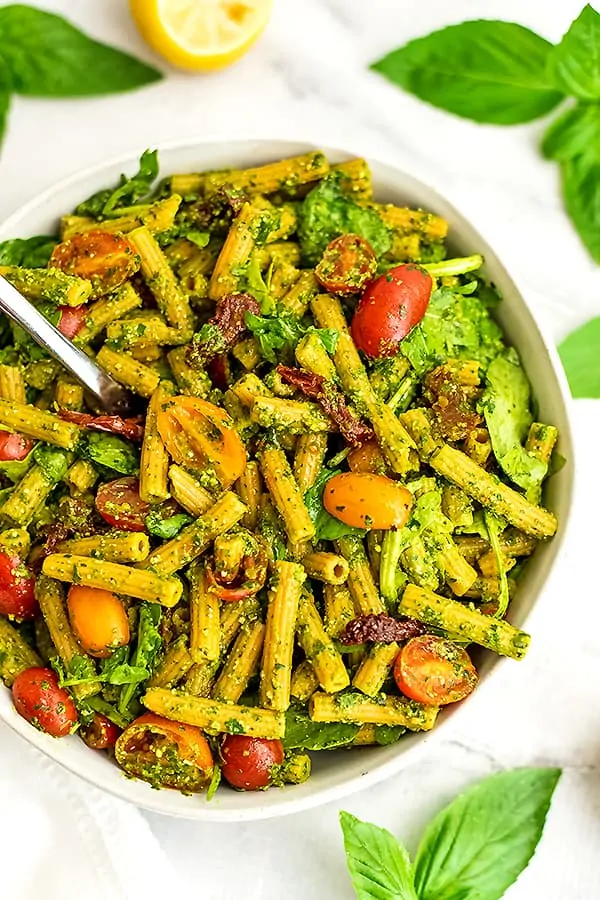 Fork in bowl of pesto pasta salad with sundried tomatoes.