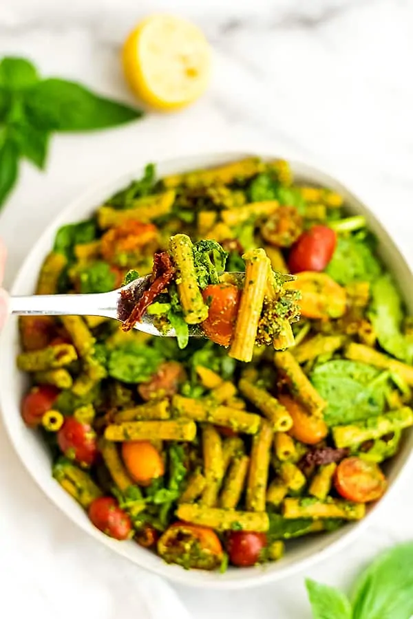 Fork full of pesto pasta salad with sun dried tomatoes.