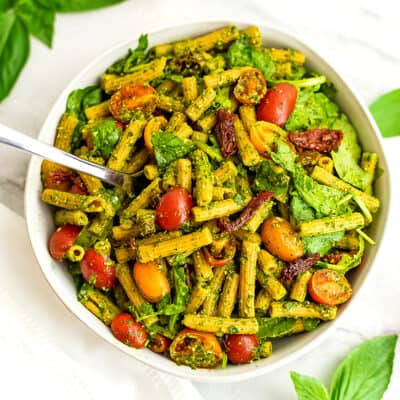 Pesto pasta salad with sun dried tomatoes with fork in the bowl.