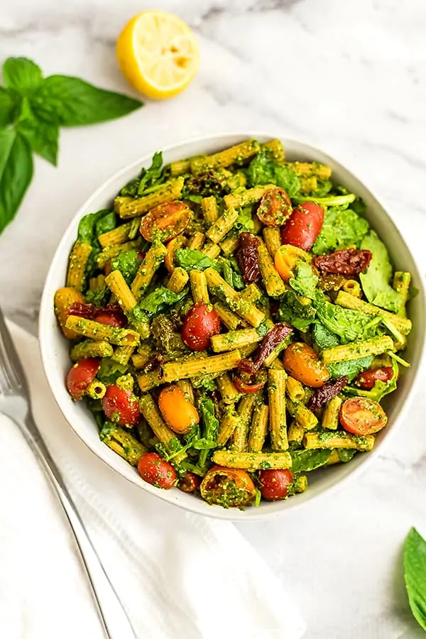 Bowl of pesto pasta with sundried tomatoes with fork on side.