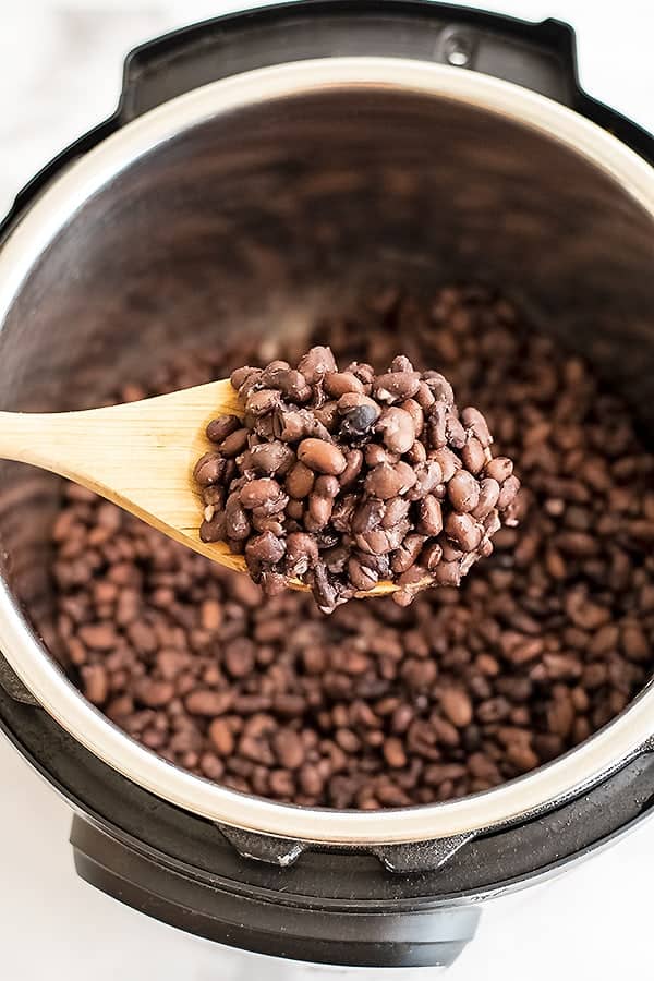 Wooden spoon filled with cooked black beans.