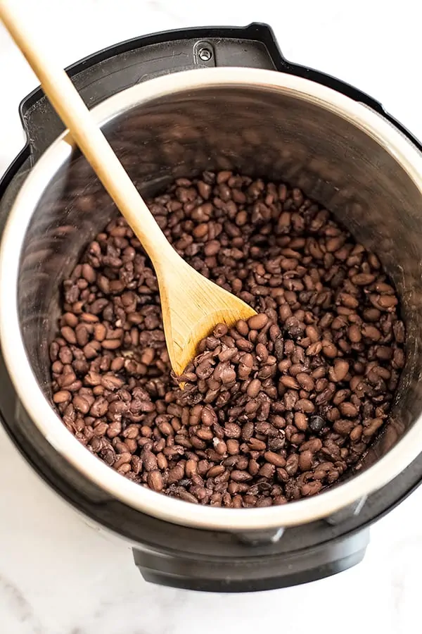 Wooden spoon in Instant Pot filled with black beans.