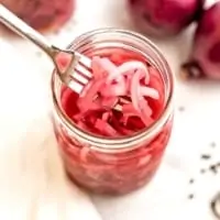Glass jar of pickled onions with a forkful of onions.