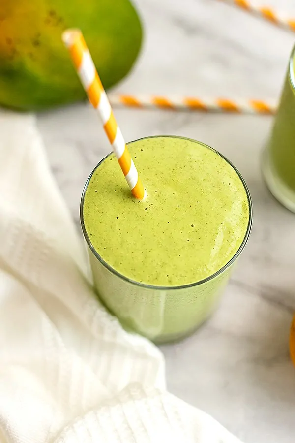 Mango kale smoothie in a bowl with a orange striped straw. 