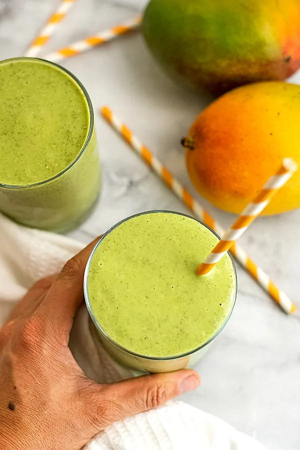 Hand holding a glass of mango kale smoothie.